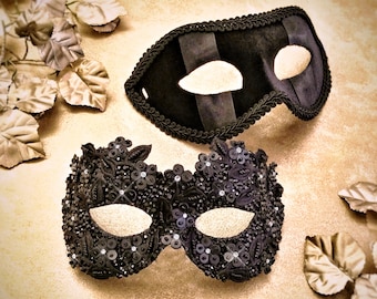 Può includere: Due maschere da ballo nere. Una maschera è in velluto con un design semplice. L'altra maschera è più elaborata e presenta paillettes e perline nere.