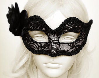 May include: A black lace masquerade mask with a black flower embellishment. The mask is worn on a mannequin with blonde hair.