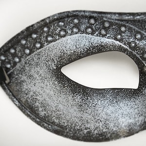 Pu&ograve; includere: Una maschera da carnevale nera con finitura glitter argentata e un solo foro per l'occhio. La maschera ha un elastico nero.