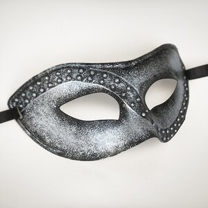 Pu&ograve; includere: Una maschera da ballo nero e argento con un'unica apertura per l'occhio. La maschera ha una superficie testurizzata ed &egrave; decorata con piccoli borchie argentate.