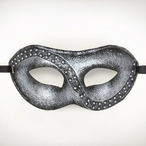 Pu&ograve; includere: Una maschera da ballo in argento e nero con un design decorativo. La maschera ha un solo foro per l'occhio ed &egrave; attaccata a un nastro nero.