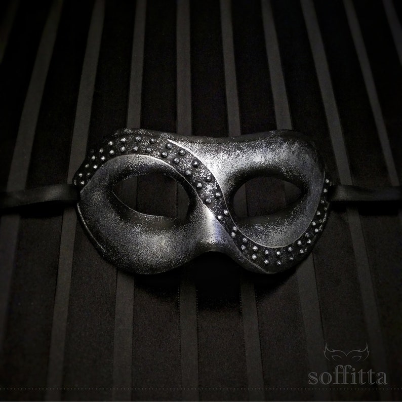Pu&ograve; includere: Una maschera argentata per un ballo in maschera con un nastro nero. La maschera ha una superficie testurizzata ed &egrave; decorata con piccoli borchie argentate.
