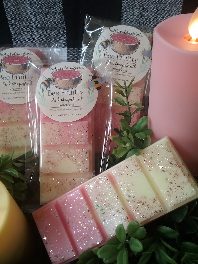May include: Three wax melts in clear packaging with pink and white glitter. The wax melts are labelled "Bee Fruitty Pink Grapefruit" and feature a bee and grapefruit illustration. The text "BeeWicked Wax Works" is also on the packaging.