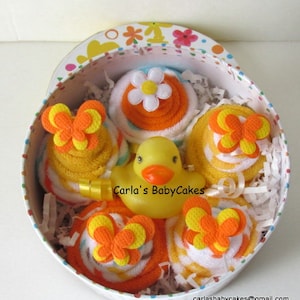 May include: A yellow rubber ducky in a gift box with four rolled up towels decorated with orange and yellow butterflies. The towels are arranged in a circle around the ducky. The box is decorated with a colorful floral pattern.