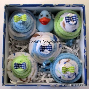 May include: A blue and white gift box filled with six baby shower favors. Each favor is a stack of blue and white towels with a green bow. The box also includes a blue rubber duck.