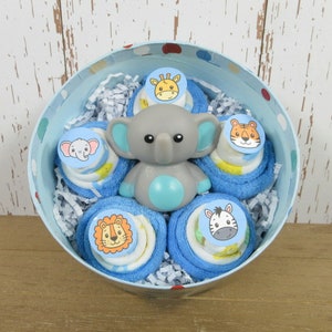May include: A blue and white polka dot tin filled with blue and white baby washcloths rolled into a flower shape. Each washcloth has a different animal face on it: a giraffe, a tiger, a zebra, an elephant, and a lion. A gray elephant bath toy is in the center of the arrangement.