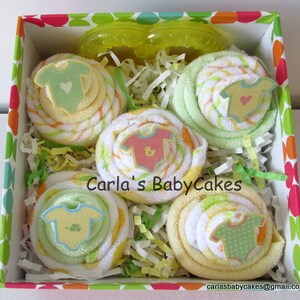 May include: A gift box filled with four yellow and green baby washcloths rolled into the shape of cupcakes. Each cupcake is topped with a small felt baby onesie. The box is lined with white shredded paper and has a colorful polka dot pattern.