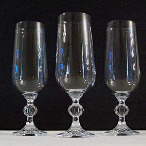 May include: Three clear glass champagne flutes with tall, slender stems and a round bowl. The flutes are on a black surface.