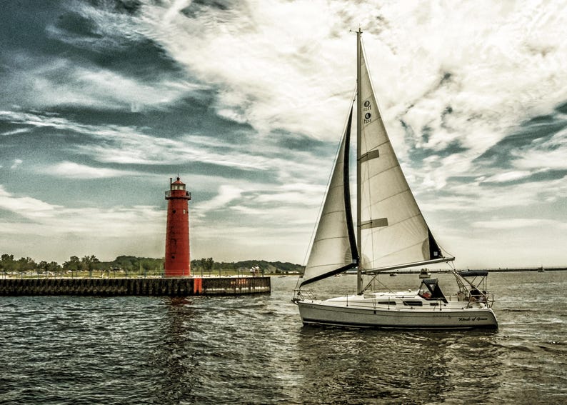 May include: A sailboat with white sails glides on the water near a red lighthouse. The sky is filled with dramatic clouds. The scene evokes a sense of tranquility and maritime adventure.