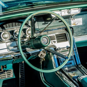 May include: Interior view of a classic car, showcasing a teal steering wheel, dashboard, and accents. The dashboard features chrome-rimmed gauges and a radio. The car's interior is a mix of teal and chrome, with a focus on vintage design.