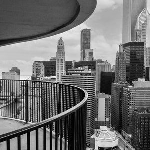 May include: A black and white photo of a city skyline viewed from a balcony with a curved railing. The balcony is on a high-rise building with a curved ceiling. The city skyline is made up of tall buildings with windows.