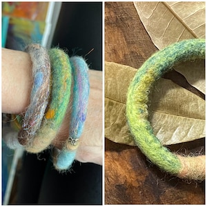 May include: A collection of colorful felted wool bracelets. The bracelets feature a variety of colors, including blue, green, and brown, with a textured, handmade appearance. One bracelet has a silver bead. The bracelets are approximately 2 inches in diameter.
