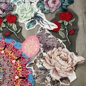 May include: A collection of assorted fabric appliques featuring floral and mandala designs. The pieces include red roses, a large pale green rose, a beige peony, purple lilac clusters, and a colorful mandala. A yellow measuring tape shows 34 inches.