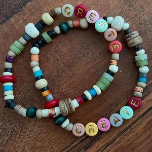 May include: Two colorful beaded bracelets with the word "CREATE" spelled out in gold letters on each bracelet.