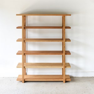 May include: A wooden bookshelf with five shelves. The bookshelf is made of light brown wood and has a simple, modern design.
