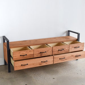May include: A wooden bench with six drawers that are open, revealing the interior. The bench is made of dark wood with black metal accents. The drawers are made of light wood and have black metal handles.