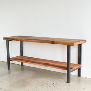 May include: A rustic wooden shelf with a black metal frame. The shelf has two tiers and is made of reclaimed wood.