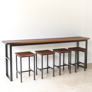 May include: A long, rectangular wooden table with a black metal frame and four matching wooden stools with black metal frames. The table and stools are all made of dark wood.