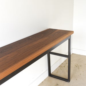 May include: A long, narrow console table with a dark wood top and black metal legs. The table has a simple, modern design and would be a great addition to any home.