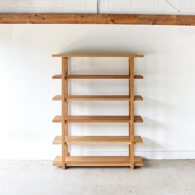 May include: A wooden bookshelf with five shelves. The bookshelf is made of light brown wood and has a simple, modern design.