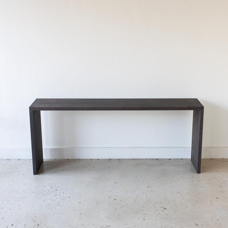 May include: A dark brown wooden console table with a rectangular top and a simple, minimalist design. The table has a sleek, modern look and would be a stylish addition to any home.