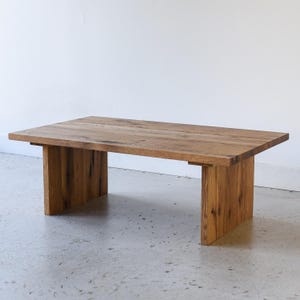 May include: A rustic wooden coffee table with a rectangular top and a simple, modern design. The table is made of reclaimed wood with a natural finish, and it has a slightly distressed look. The table is supported by four legs that are attached to the underside of the top.