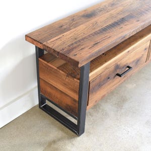 May include: A rustic wooden media console with two drawers and a black metal frame. The console has a distressed wood finish and a simple design.