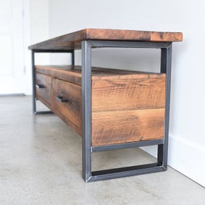 May include: A rustic wooden media console with a black metal frame and two drawers. The console has a distressed wood finish and a simple, modern design.