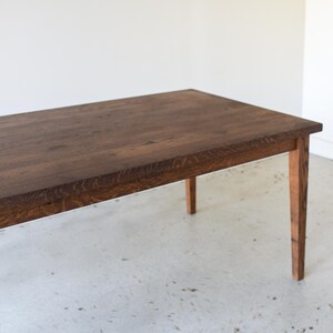 Op de afbeelding: Een rechthoekige houten tafel met een donkerbruine afwerking. De tafel heeft vier poten en een eenvoudig, strak ontwerp. De houtnerf is zichtbaar op het tafelblad. De tafel is ongeveer 183 cm lang.