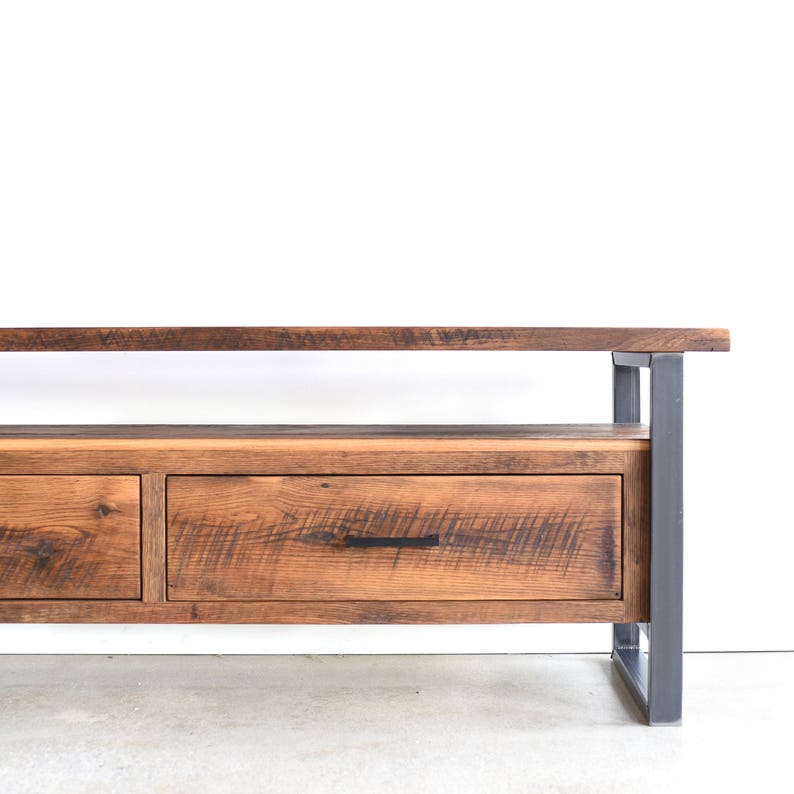 May include: A rustic wooden media console with two drawers and a shelf. The console has a dark brown stain and is made of reclaimed wood. The metal legs are black.
