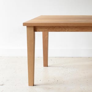 Op de afbeelding: Een lichtgekleurde houten tafel met een rechthoekig blad en vier stevige, vierkante poten. De tafel is gemaakt van natuurlijk hout, dat de nerf en textuur laat zien. Het ontwerp is eenvoudig en modern, geschikt voor diverse interieurstijlen.