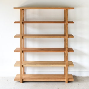 May include: A wooden bookshelf with five shelves. The bookshelf is made of light brown wood and has a simple, modern design.