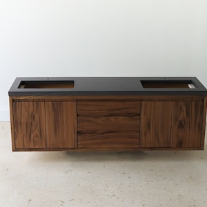 May include: A double vanity bathroom sink with a dark gray countertop and walnut wood cabinets. The sink has two separate basins.