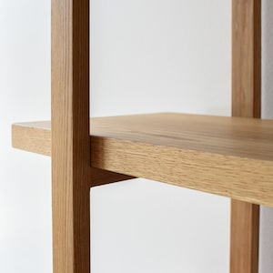 May include: Close-up of a wooden shelf unit with a light brown finish. The shelf is made of solid wood and has a simple, modern design.