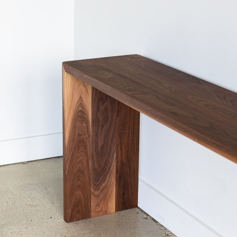 May include: A dark brown wooden console table with a rectangular top and a simple, modern design. The table is made of solid walnut wood and has a natural finish.