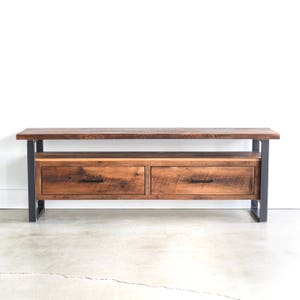 May include: A rustic wooden media console with two drawers and a lower shelf. The console has a dark brown wood finish and black metal legs.