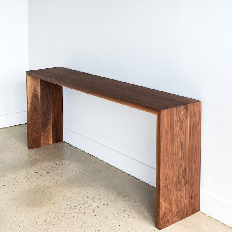 May include: A long, narrow console table made of dark walnut wood. The table has a simple, modern design with a rectangular top and a unique, open frame.