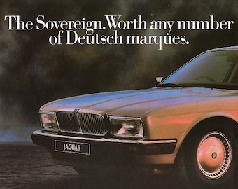 May include: A silver Jaguar Sovereign sedan with a chrome grille and the text "The Sovereign. Worth any number of Deutsch marques." and "JAGUAR" on the front bumper.
