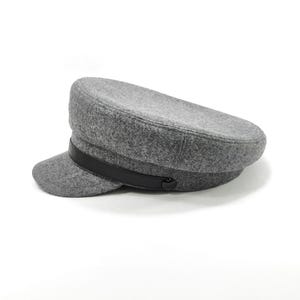 May include: A gray wool hat with a black leather band and a small brim. The hat has a classic, structured design, suitable for various styles. The hat is a neutral color, making it versatile for different outfits.
