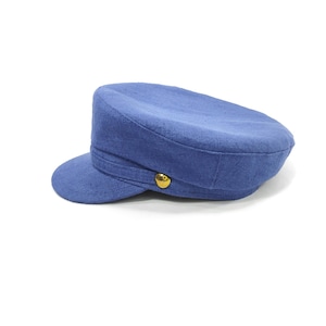 May include: A blue cadet hat with a short brim and a rounded crown. The hat features a gold-colored button on the side and a matching fabric band. The hat is made of a textured fabric and is set against a white background.