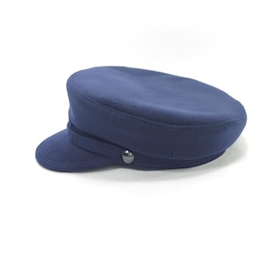 Peut inclure: Un chapeau bleu marine avec une petite visière et une couronne arrondie. Le chapeau a une bande autour de la couronne et un bouton argenté. Ce chapeau est un style classique, adapté à diverses occasions.