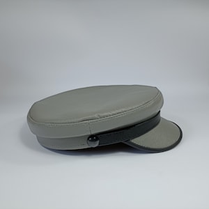 May include: A grey leather cap with a black leather band and a black button. The cap has a slightly curved brim.
