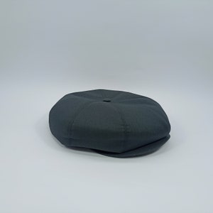 May include: A dark gray newsboy cap with a rounded crown and a brim that curves down on the sides.