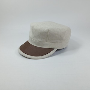 May include: A beige linen cap with a brown brim. The cap has a flat top and a slightly curved brim.