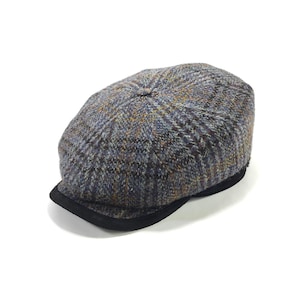 May include: A tweed newsboy cap in shades of grey, blue, and brown, featuring a black brim. The cap's fabric has a textured appearance. This classic hat is suitable for various occasions.