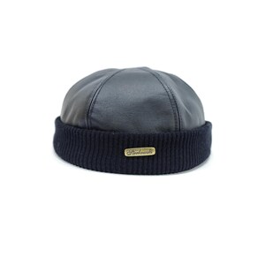 May include: A navy blue beanie hat with a leather crown and a ribbed knit brim. A small gold-coloured rectangular tag with the word "Sterkowski" is sewn on the brim. The hat is set against a white background.