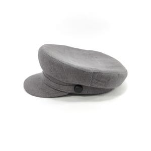 May include: A gray, flat-brimmed hat with a rounded crown and a small, curved brim. The hat features a dark button detail and a band around the crown. The hat is made of a textured fabric.