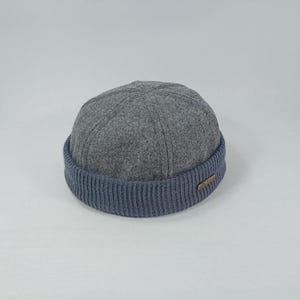 May include: A grey wool beanie with a blue ribbed cuff. The beanie has a rounded shape and a simple design.