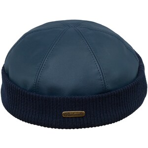 May include: A navy blue leather beanie hat with a ribbed knit brim. The top of the hat is stitched in a panel design. A small, rectangular gold-toned metal tag with the brand name is on the brim.