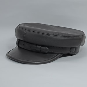 May include: A black leather cap with a wide brim and a strap with a buckle. The cap has a stitched design and a slightly rounded crown.